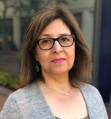 A woman with glasses and brown hair wearing a gray sweater.